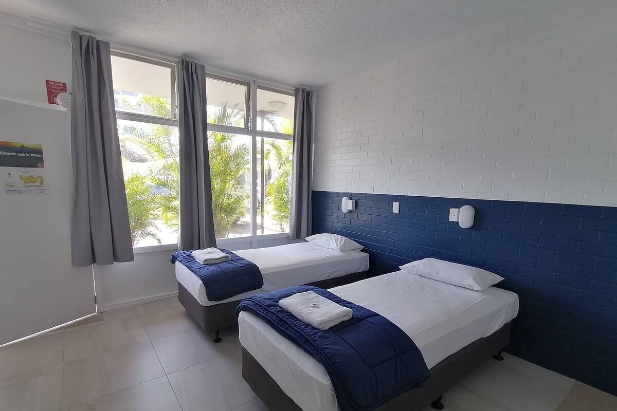 A hotel room with two beds, a window with curtains, a white brick wall, and a check-out time sign.