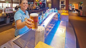 A bar area with a long counter, multiple taps, and a person holding a beer glass. - Hoey Moey Backpackers - Hostel (Coffs Harbour)