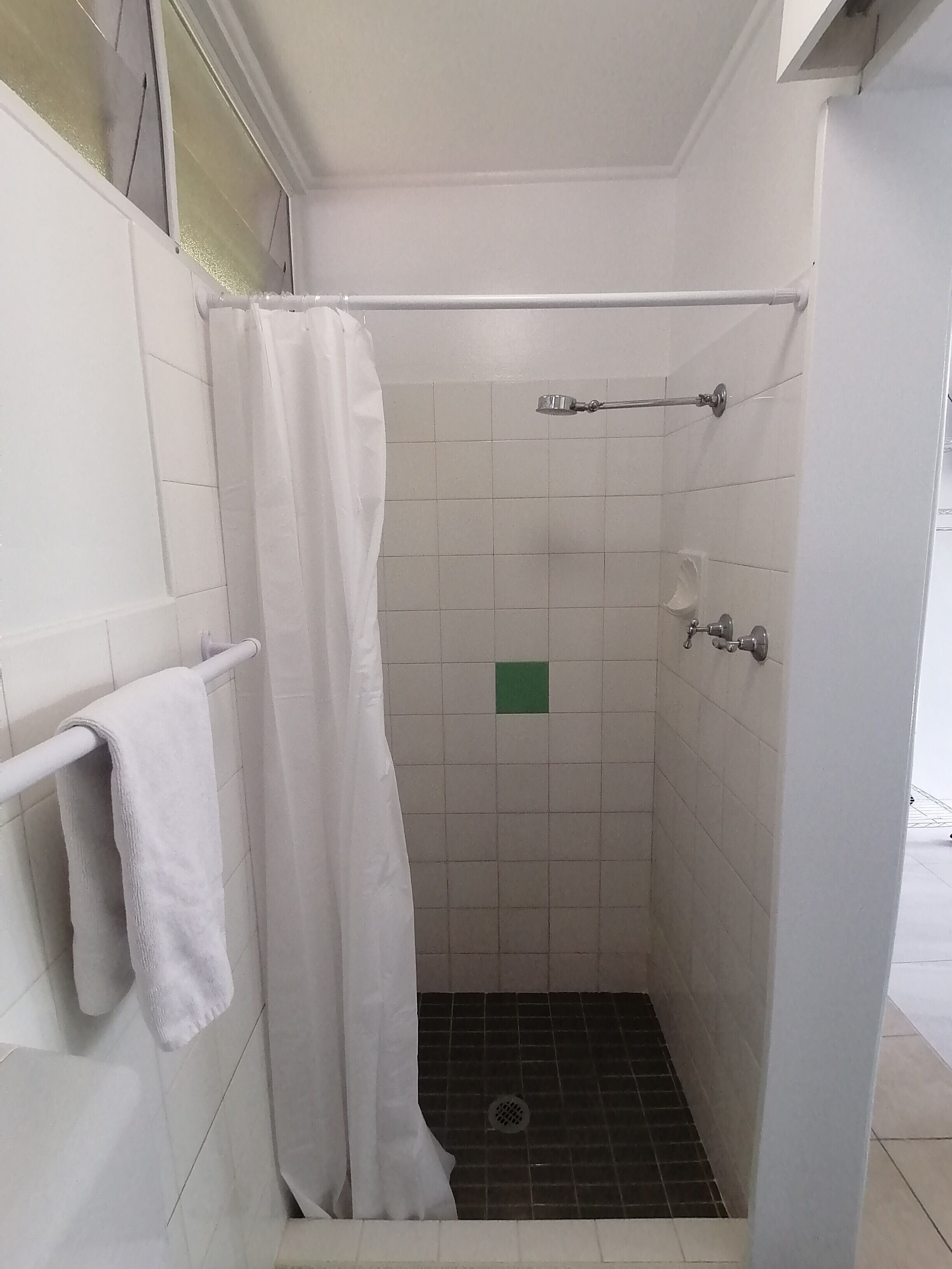 A small, enclosed shower area with white tiles, a towel rack, and a green square tile on the wall.
