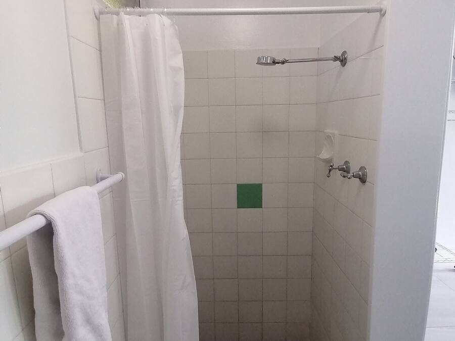 A small, enclosed shower area with white tiles, a towel rack, and a green square tile on the wall.