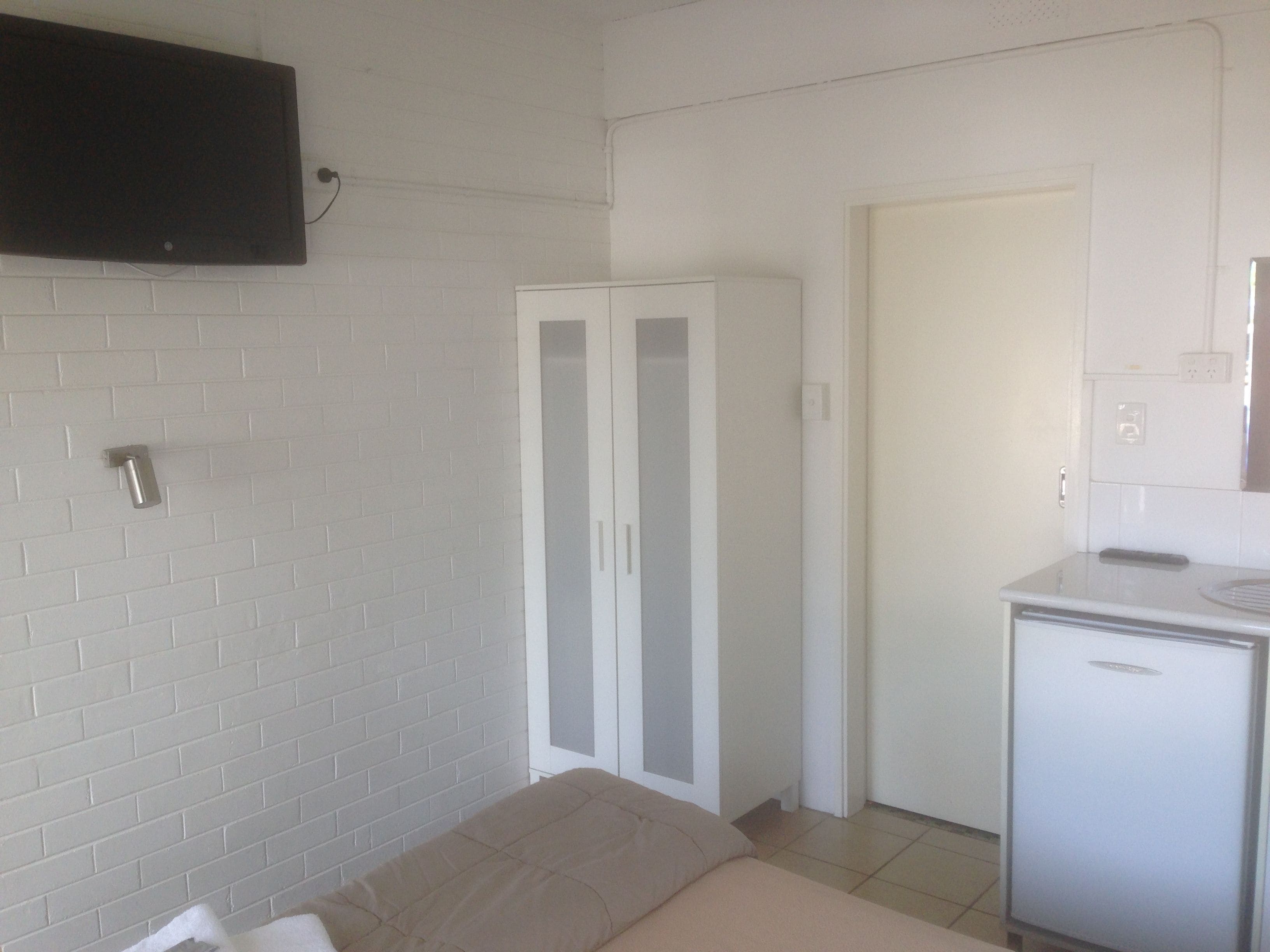 A room with a bed, a wardrobe, a small kitchenette, and a TV mounted on the wall.
