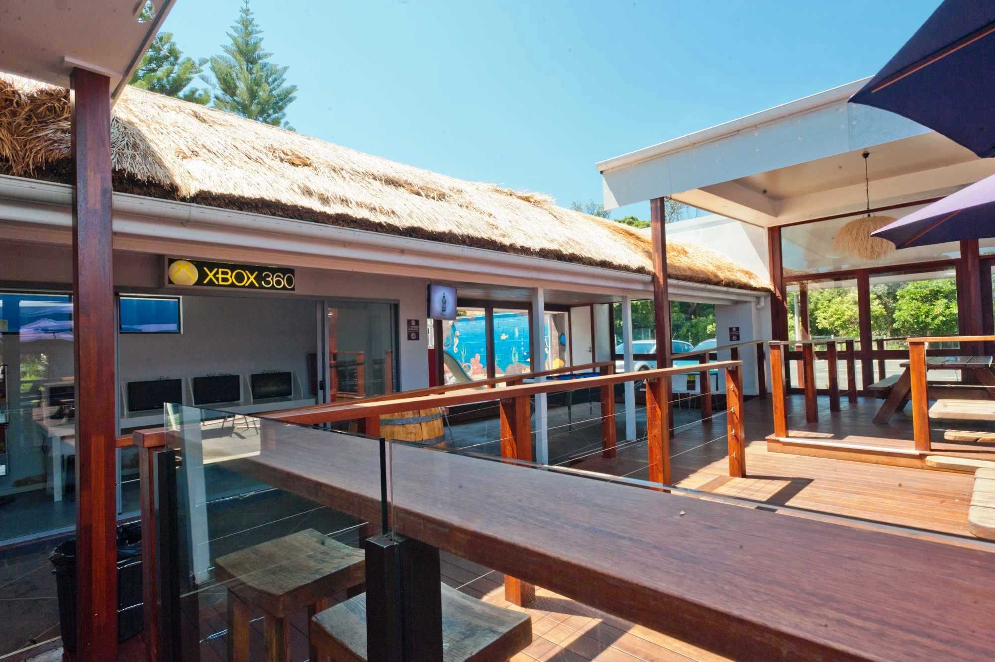 A beachside restaurant with a thatched roof, wooden deck, and glass railings.