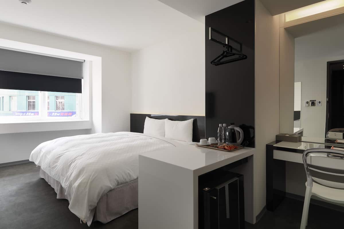 A modern hotel room with a bed, bedside table, and a small desk with a chair.