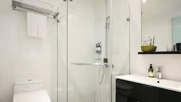 Een moderne badkamer met een douche in een glazen cabine, een wit toilet, een zwarte wastafel en een spiegel boven de wastafel.
