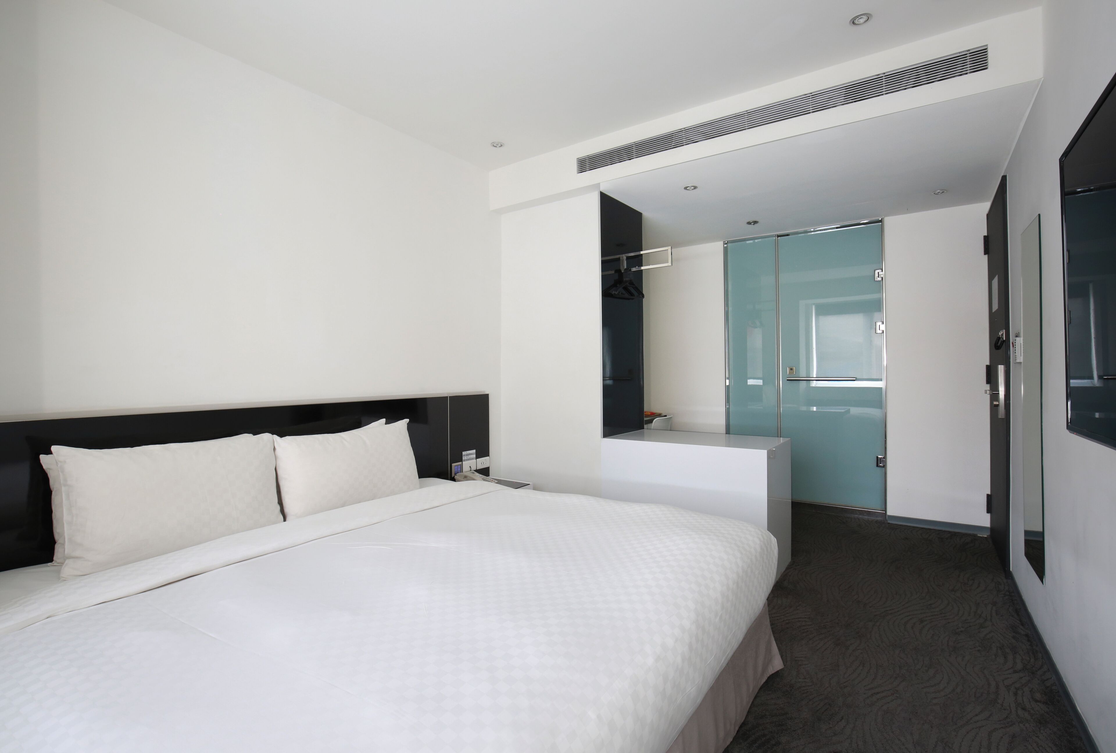 A modern hotel room with a large bed, a walk-in closet, and a bathroom with a glass shower.