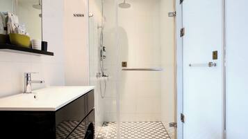 Un baño moderno con ducha de vidrio, lavamanos blanco y piso a cuadros.