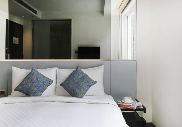 A hotel room with a bed, two decorative pillows, a nightstand with a cup and a book, and a large mirror above the bed. - Cityinn Hotel Plus - Taichung Station Branch (Taichung)