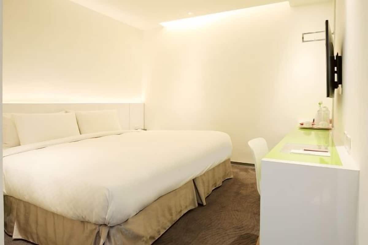 A hotel room with a bed, a desk, and a TV mounted on the wall.