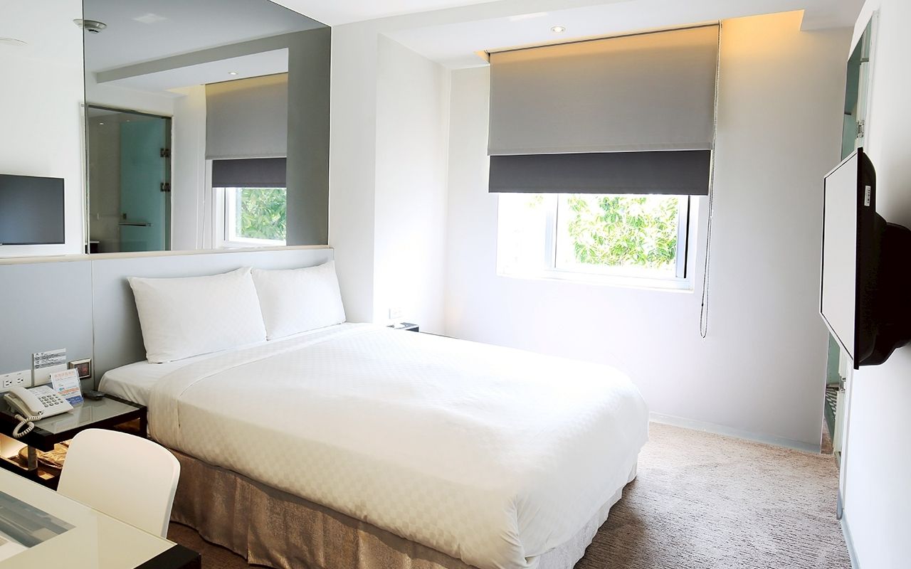 Quarto de hotel moderno com uma cama grande, uma escrivaninha com telefone, um espelho, uma janela com vista e uma televisão.