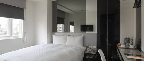 Una habitación de hotel moderna con una cama grande, un escritorio con silla, un teléfono y un espejo.