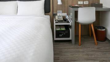 Habitació d'hotel amb llit, escriptori, cadira, paperera i una cuineta petita.