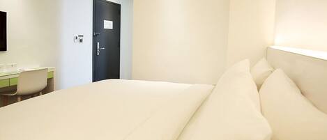 A hotel room with a bed, a desk, and a door.