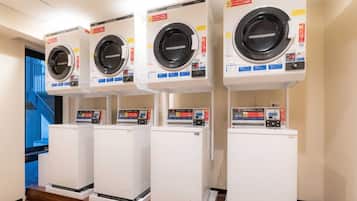 A row of white laundry machines with control panels, a blue staircase in the background, and a wooden floor.