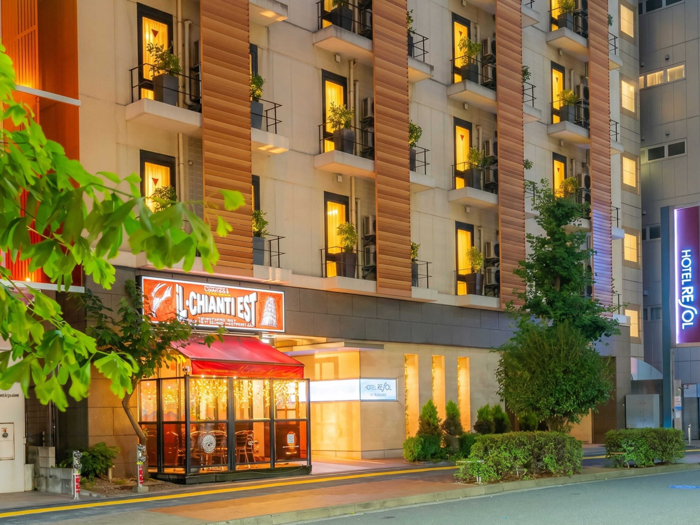 A hotel with a modern facade, multiple balconies, and a restaurant with a red awning.