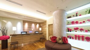 A modern reception area with a wooden reception desk, a large cylindrical column, and a display of pink flowers. - Hotel Resol Ikebukuro (Tokyo)