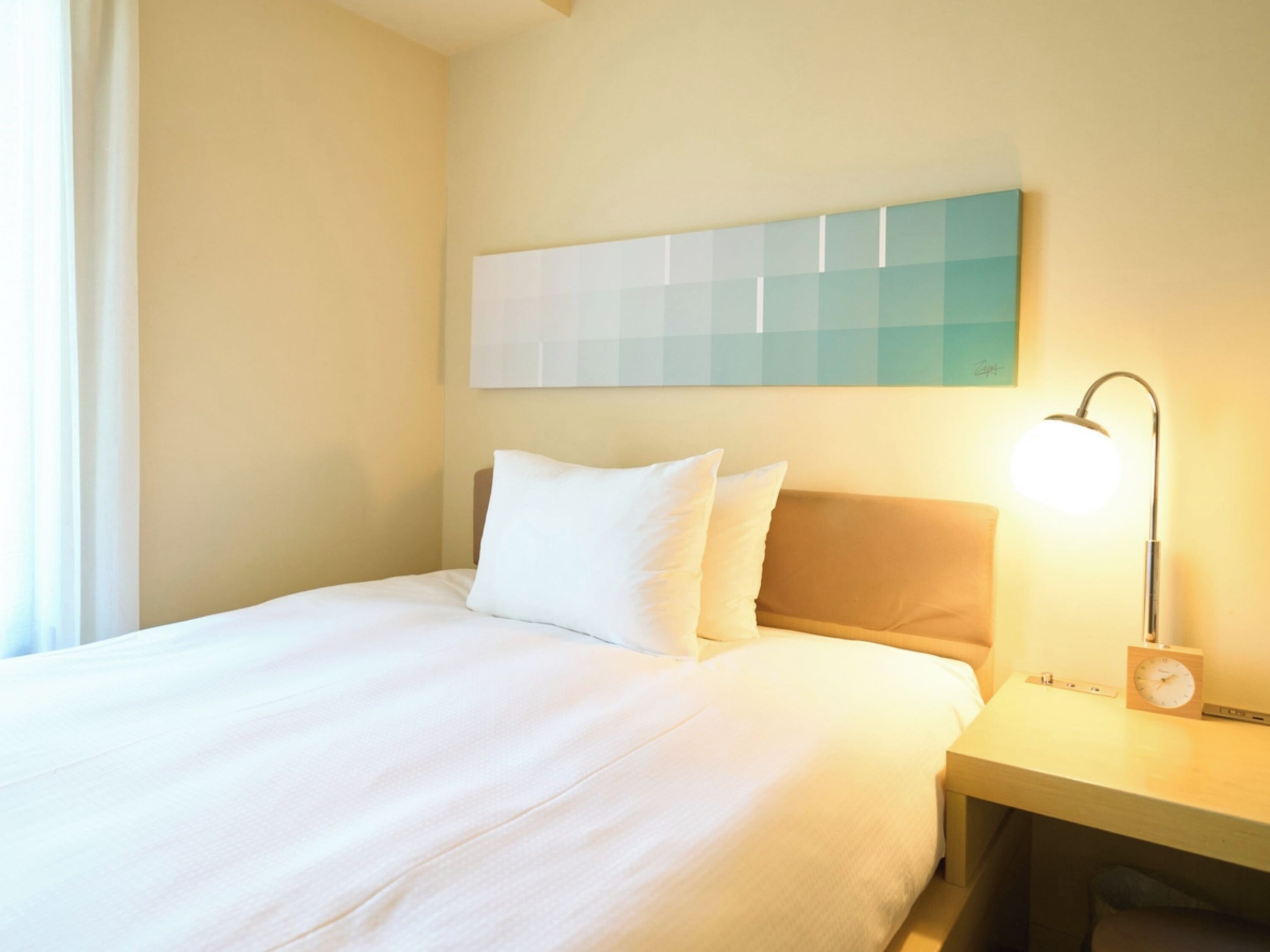 A hotel room with a bed, a nightstand, a lamp, and a wall-mounted artwork.