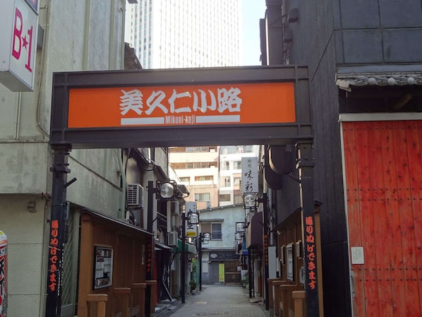 Une rue étroite, bordée de bâtiments des deux côtés, avec une porte rouge sur la droite et une enseigne au-dessus de la rue.