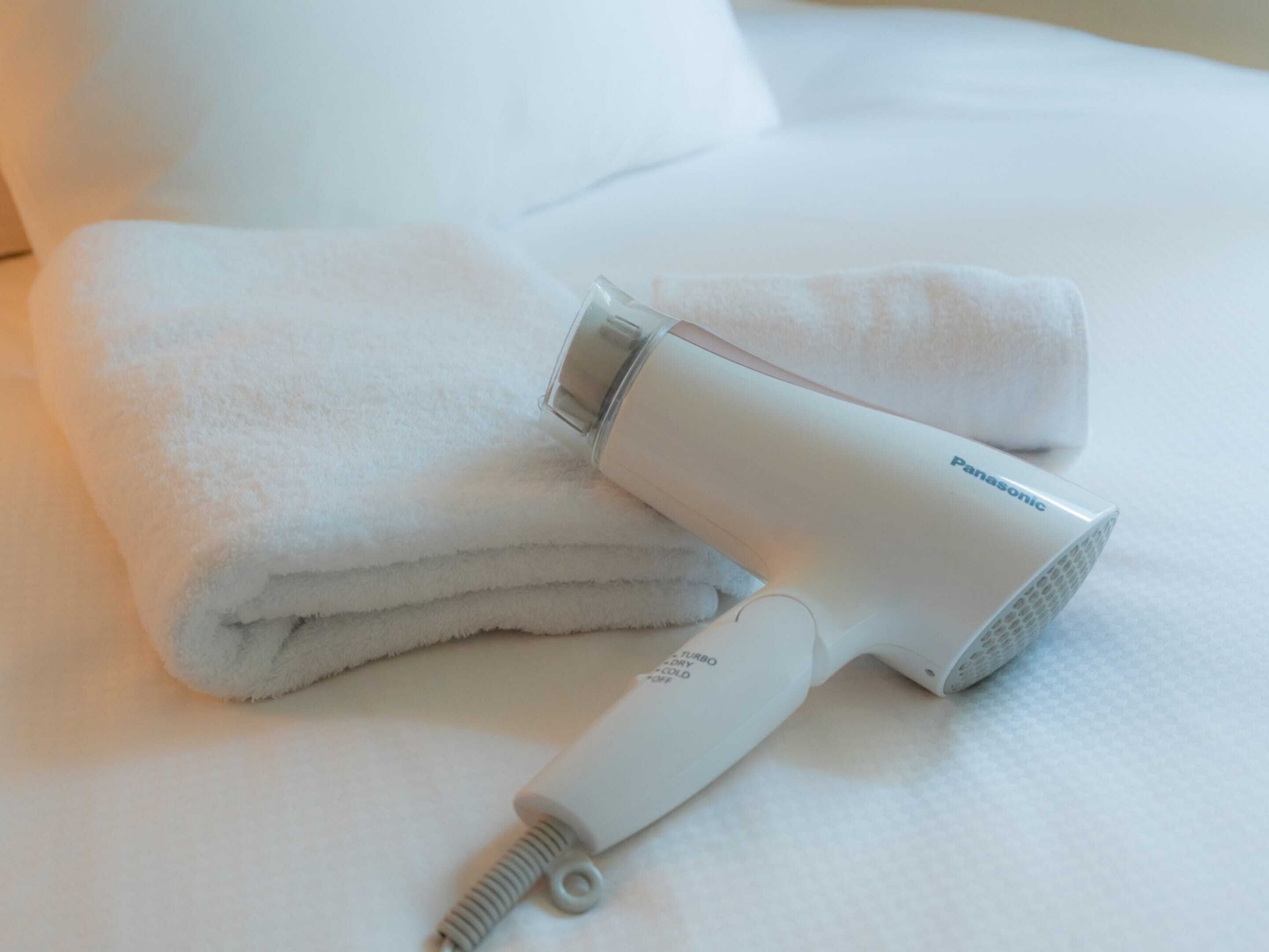 A white Panasonic hair dryer on a bed with a folded white towel.