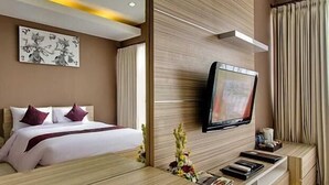 A modern hotel room with a bed, a mounted TV, and a wooden console table with a vase of flowers. - Parkside DenBukit Residence & Suite Jimbaran (Jimbaran)