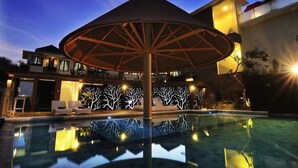 A modern pool area with a unique umbrella structure, a well-lit building, and a decorative wall with tree designs. - Parkside DenBukit Residence & Suite Jimbaran (Jimbaran)