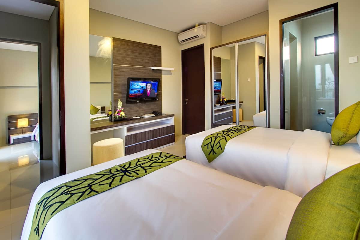 A hotel room with two beds, a TV on a stand, a mirror, and a door.
