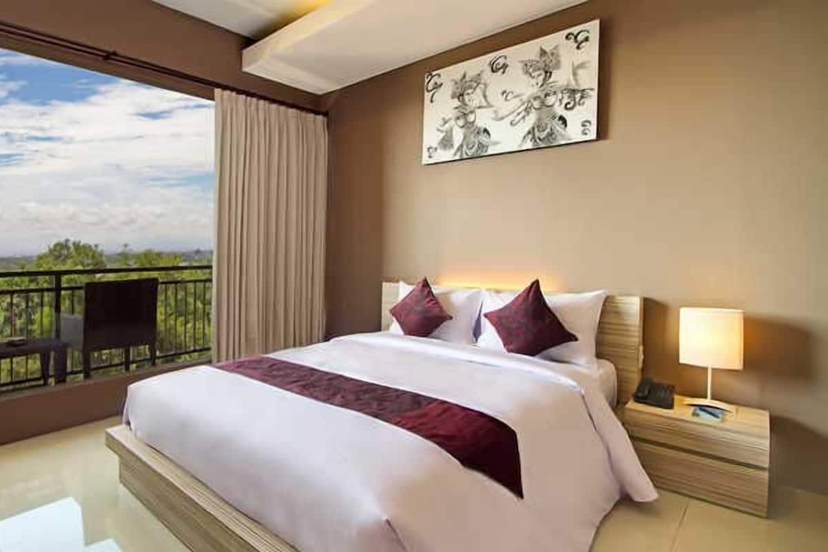 A hotel room with a large bed, a nightstand, a lamp, a painting on the wall, and a balcony with a chair.