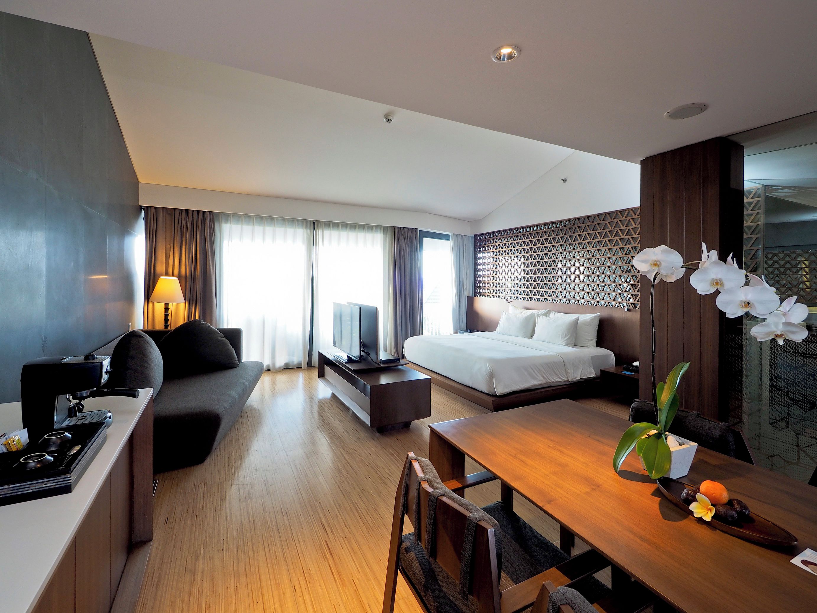 A modern hotel room with a bed, sofa, desk, and dining table.