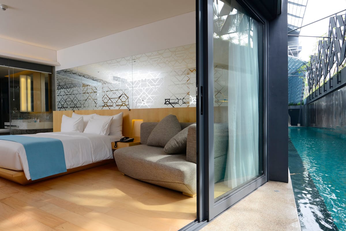 A modern hotel room with a large bed, a sofa, a glass-enclosed pool, and a geometric wall design.