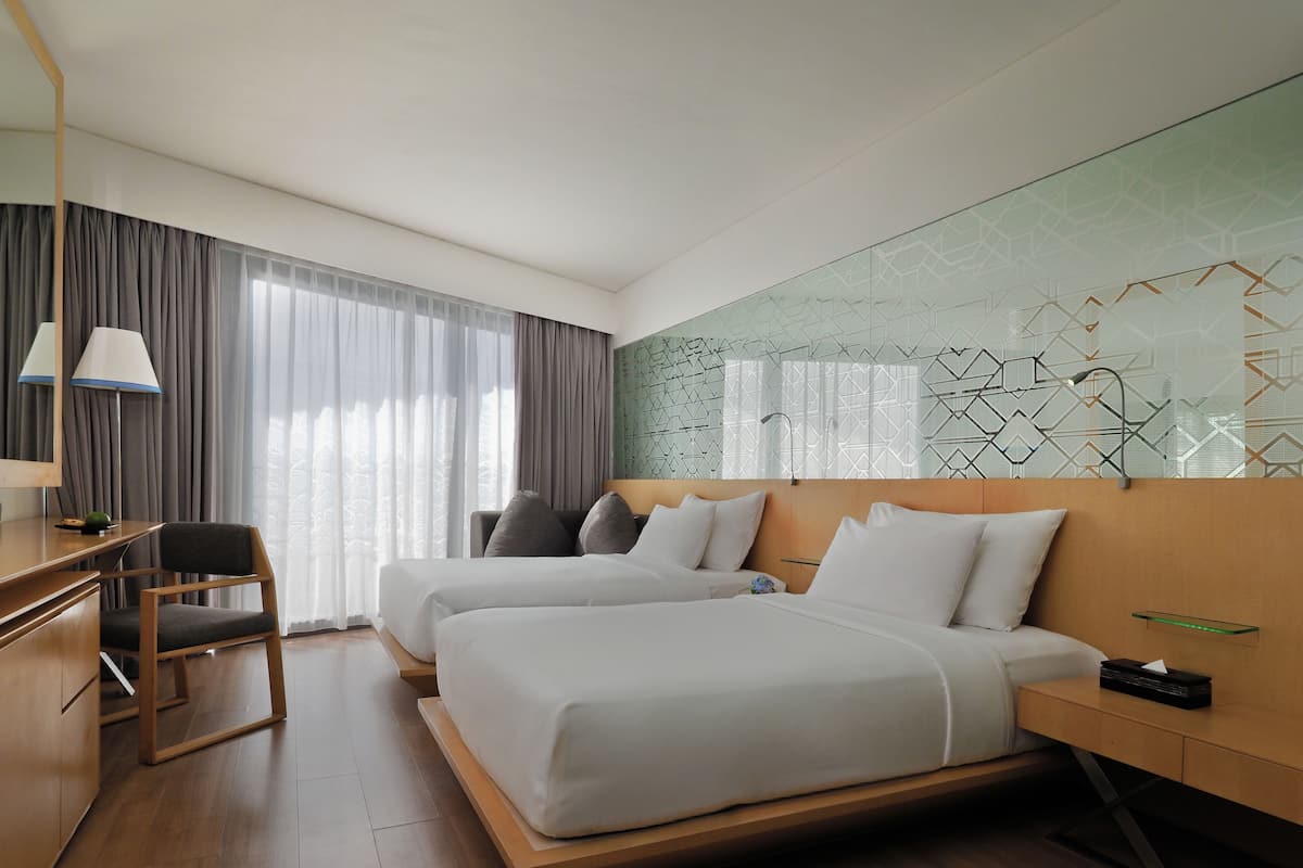 A modern hotel room with two beds, a desk, a chair, and a large window with curtains.
