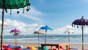 A beach with colorful umbrellas and bean bags. - IZE Seminyak by LifestyleRetreats (Seminyak)