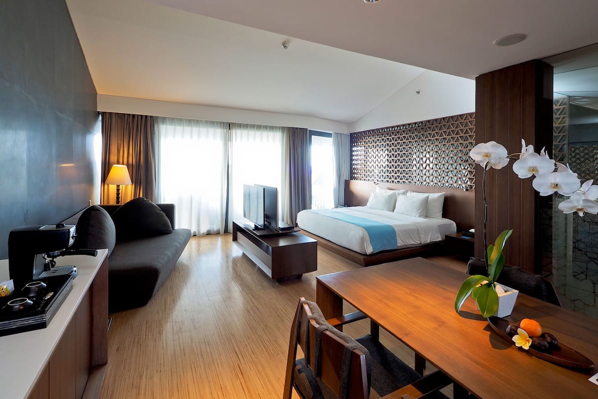 A modern hotel room with a bed, a sofa, a dining table, and a TV.