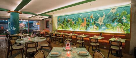 Um restaurante com mesas redondas, cadeiras e um mural com animais na parede.