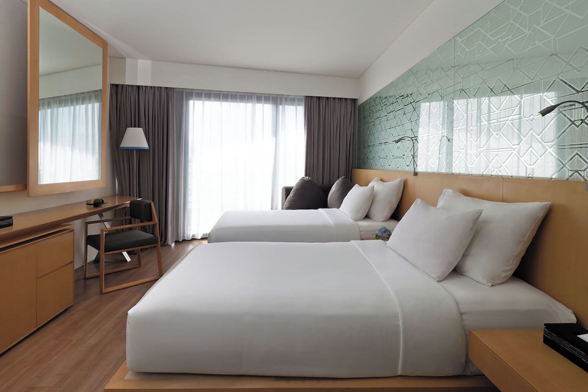 A hotel room with a large bed, a desk, a chair, a lamp, and a large mirror.