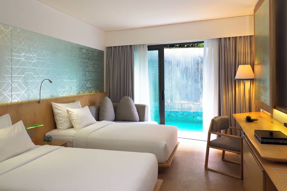 A hotel room with two beds, a desk, a chair, a TV, and a view of a pool through a glass door.