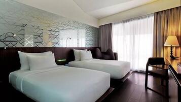 A hotel room with two beds, a desk with a chair, a lamp, and a window with curtains.