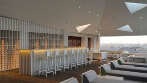 A modern bar area with a wooden floor, white bar stools, and a seating area with grey sofas and a small table. - IZE Seminyak by LifestyleRetreats (Seminyak)