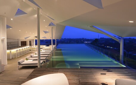 A modern hotel lobby with a pool area, seating, and a view of the city at dusk.