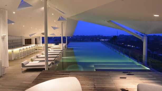 A modern hotel lobby with a pool area, seating, and a view of the city at dusk. - IZE Seminyak by LifestyleRetreats (Seminyak)