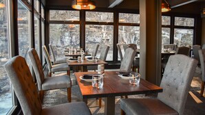 A dining area with tables set for four, large windows, and a view of trees. - Ledges Hotel (Hawley)