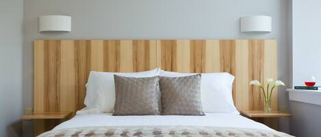 Ein ordentlich bezogenes Bett mit einer gemusterten Tagesdecke, zwei Kissen mit geometrischem Muster und einem Holz-Kopfstück.
