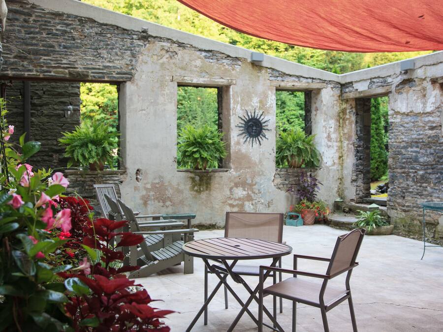 Une terrasse extérieure avec une table ronde et deux chaises, entourée de murs en pierre et de plantes en pot.
