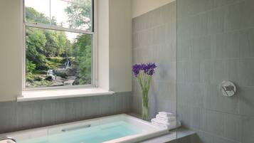 A bathroom with a bathtub, a window overlooking a waterfall, and a vase with purple flowers.