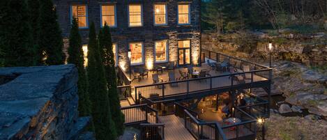 A multi-story building with a deck and outdoor seating area, surrounded by natural landscape.