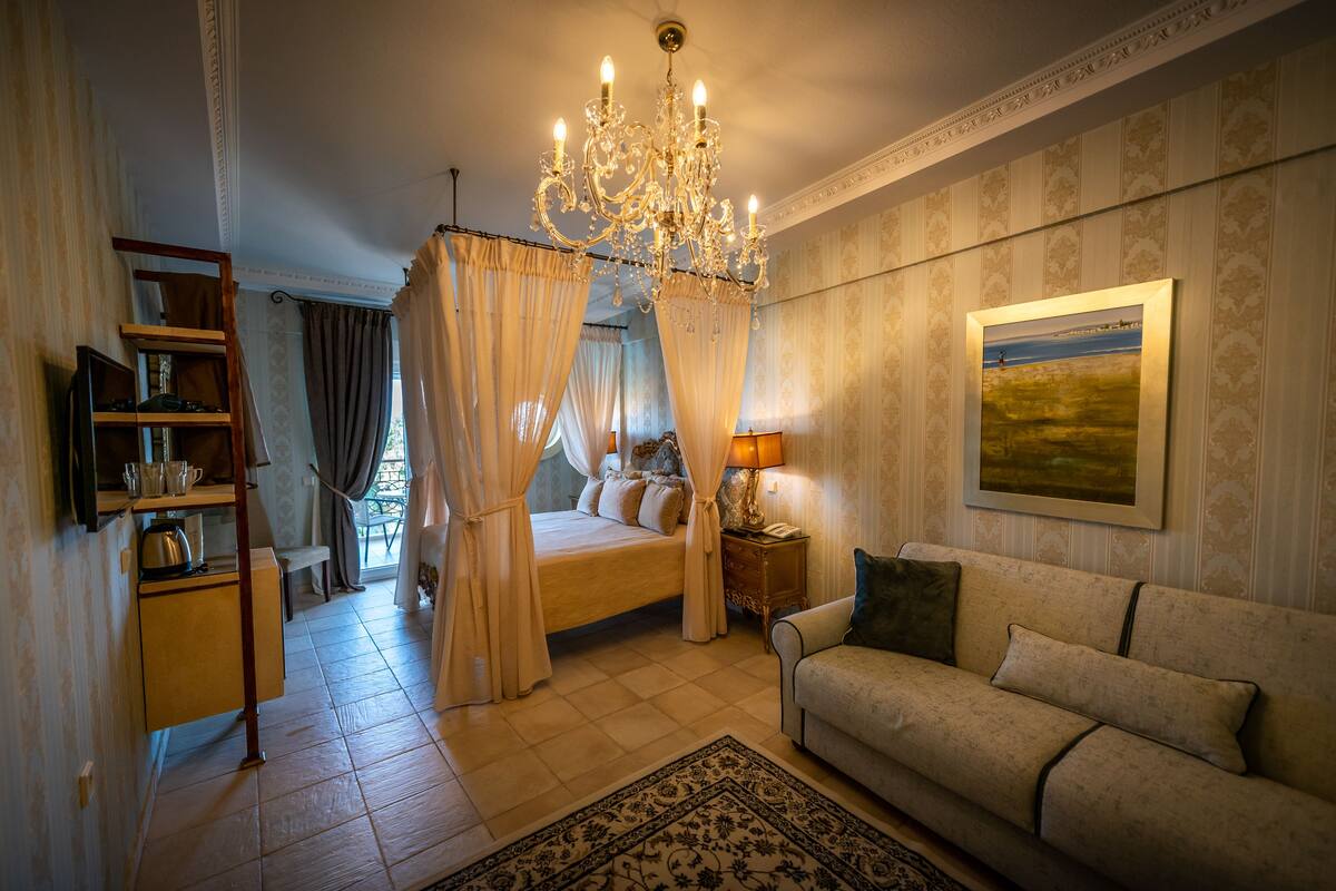 Et soveværelse med seng, sofa, lysekrone, natbord og et maleri på væggen.