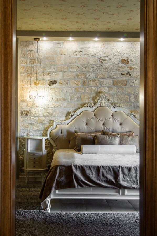 A bedroom with a stone wall, a tufted headboard, a bedside table, and a lamp. - Achtis Boutique Hotel (Kassandra)