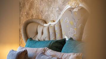 Un dormitorio con cabecera capitonada, papel tapiz floral y varios almohadones.