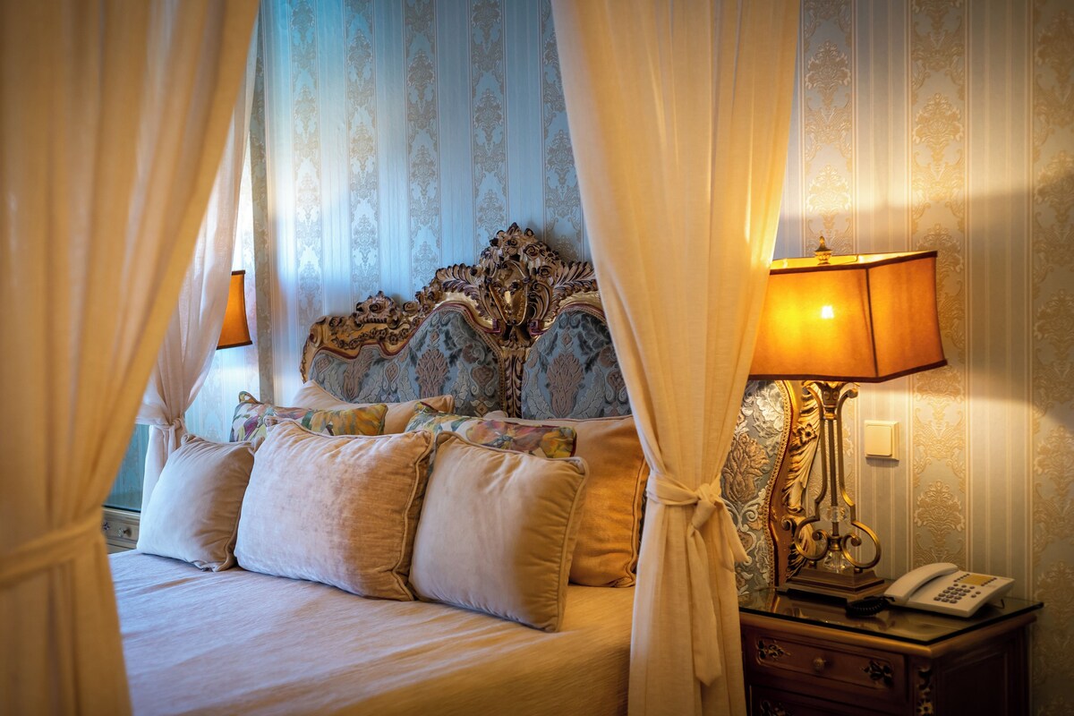 A bed with a canopy, a bedside lamp, and a telephone on a nightstand.