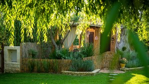 A rustic garden with a wooden fence, stone walls, and a small wooden structure with a thatched roof. - Achtis Boutique Hotel (Kassandra)