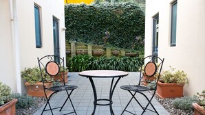 A patio with a round table and two chairs, surrounded by potted plants and a hedge. - Bella Vista Motel Wellington (Wellington)