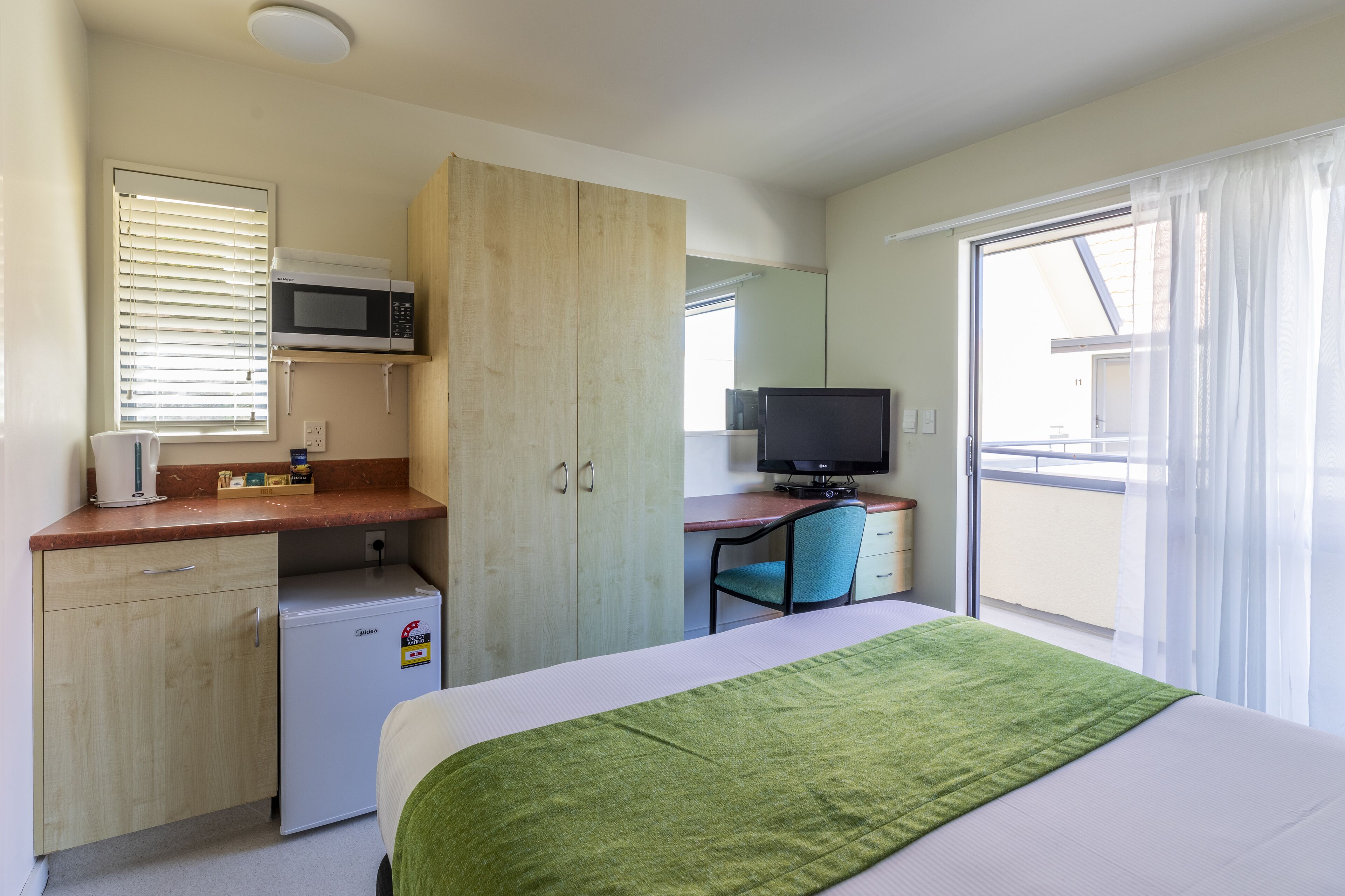 Una habitación de hotel con una cama, un escritorio con una computadora, un microondas y un refrigerador pequeño.